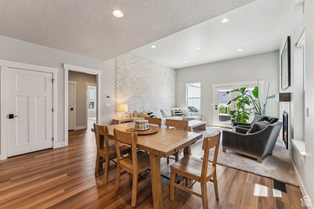 Dining area with wood finished floors, a lit fireplace, recessed lighting, baseboards, and a textured ceiling