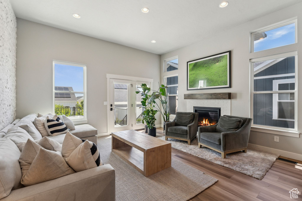 Living area with a brick fireplace, plenty of natural light, recessed lighting, wood finished floors, and baseboards
