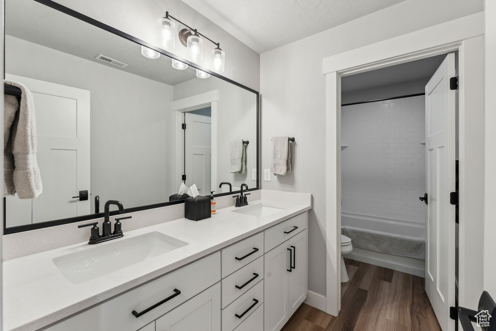 Full bath featuring toilet, double vanity, wood finished floors, shower / bathtub combination, and baseboards
