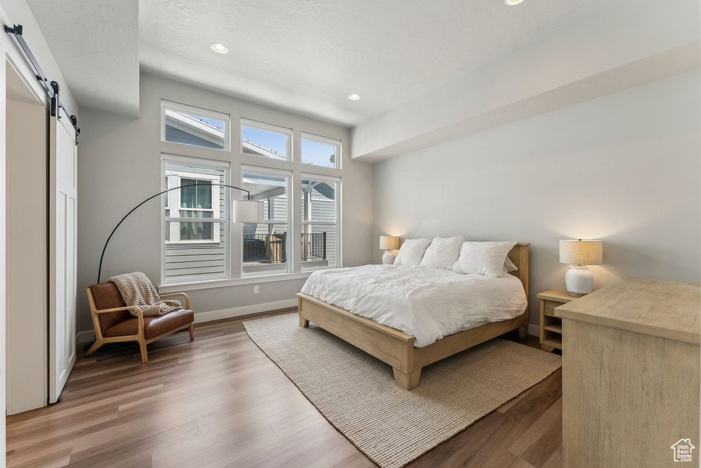 Bedroom with a barn door, recessed lighting, wood finished floors, and baseboards