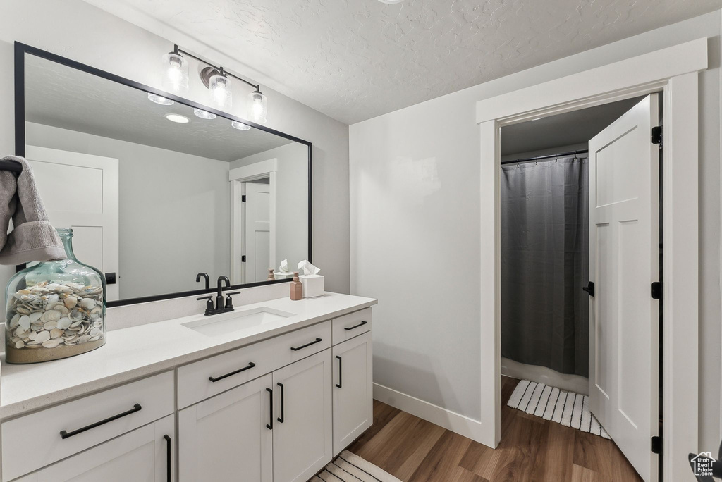 Bathroom with wood finished floors, vanity, a textured ceiling, baseboards, and a shower with shower curtain