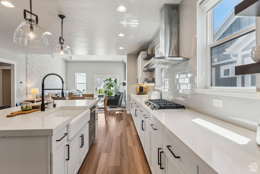 Kitchen with wall chimney range hood, a sink, appliances with stainless steel finishes, light countertops, and recessed lighting