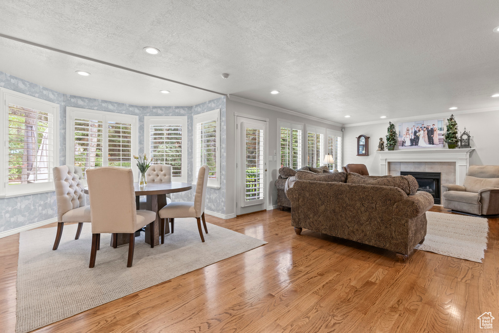 Dining area with plenty of natural light, baseboards, a tiled fireplace, light wood-style flooring, and a textured ceiling