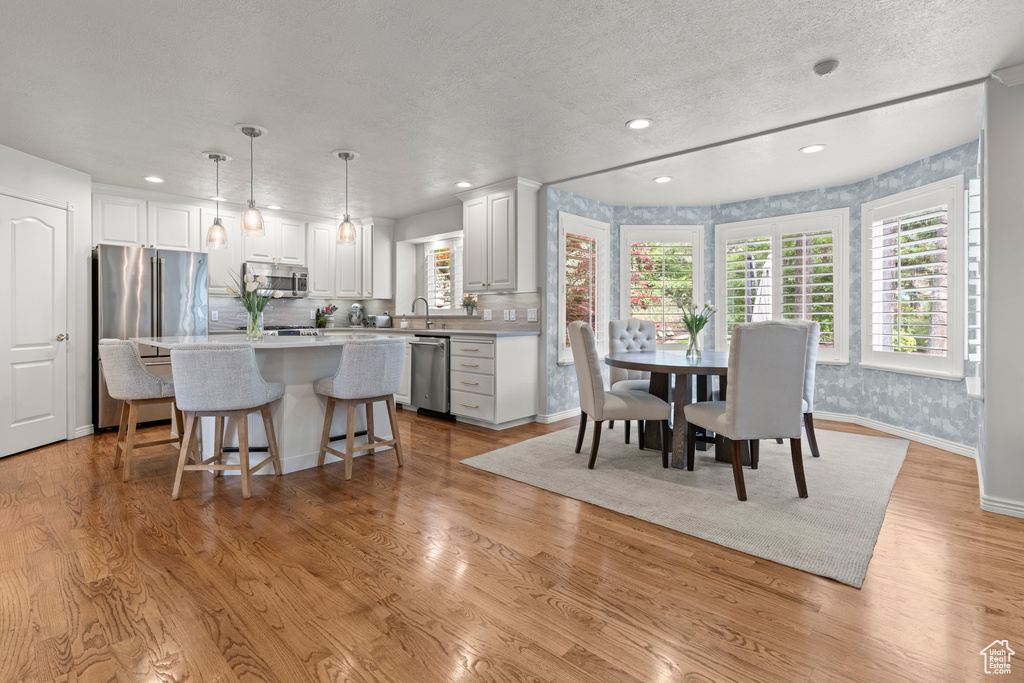 Dining area with recessed lighting, a textured ceiling, light wood-style floors, baseboards, and wallpapered walls