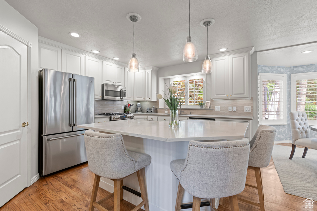 Kitchen with appliances with stainless steel finishes, recessed lighting, light wood-type flooring, a kitchen breakfast bar, and white cabinetry