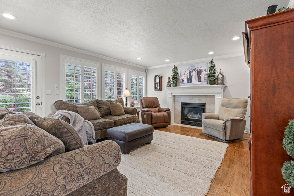 Living area featuring ornamental molding, recessed lighting, a tiled fireplace, light wood-type flooring, and a textured ceiling