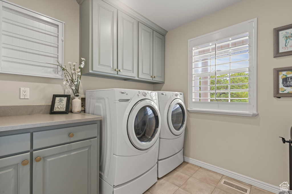 Washroom with cabinet space, independent washer and dryer, baseboards, and light tile patterned floors
