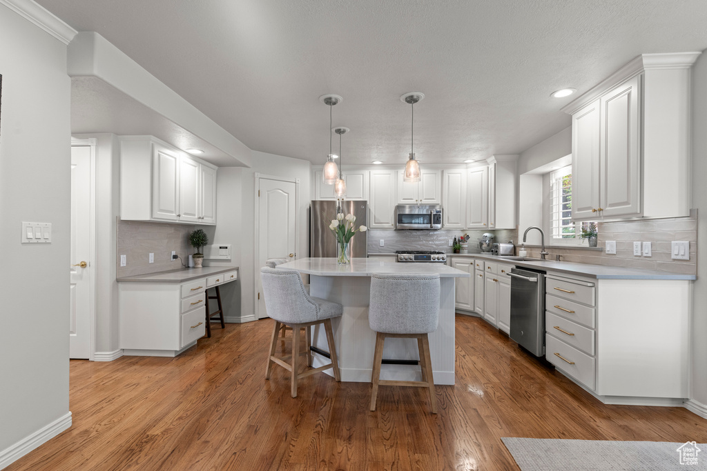Kitchen with stainless steel appliances, a sink, a kitchen bar, white cabinetry, and decorative backsplash