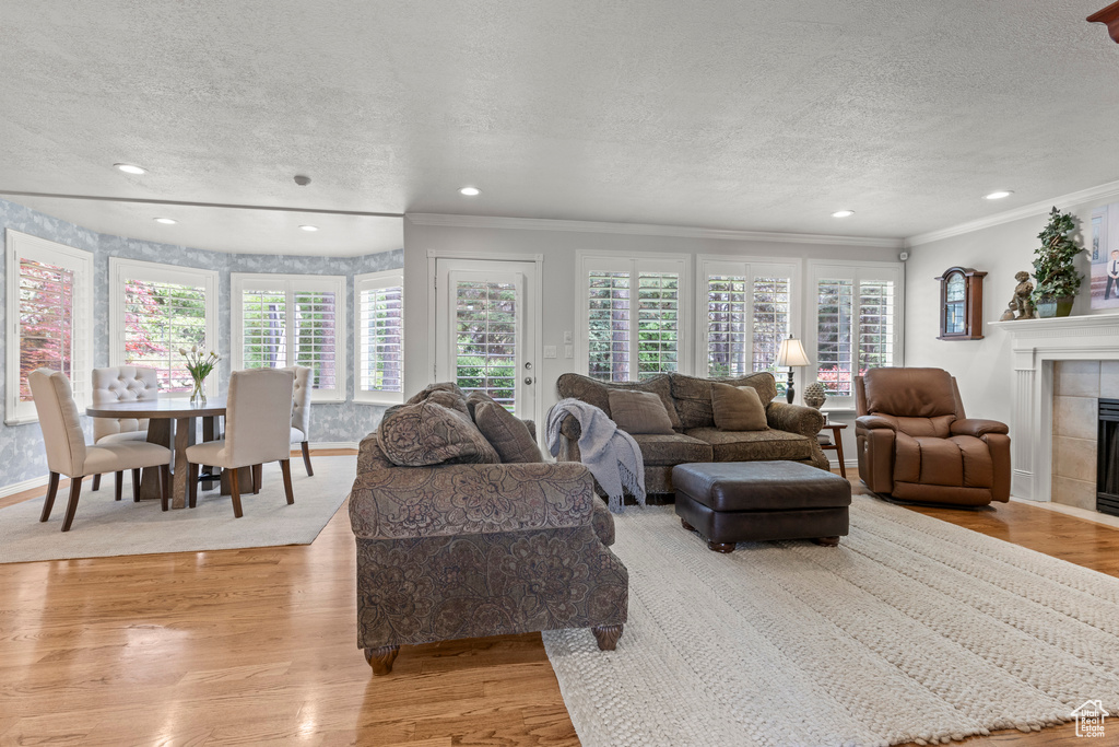 Living room with a textured ceiling, ornamental molding, a fireplace, light wood-style floors, and recessed lighting