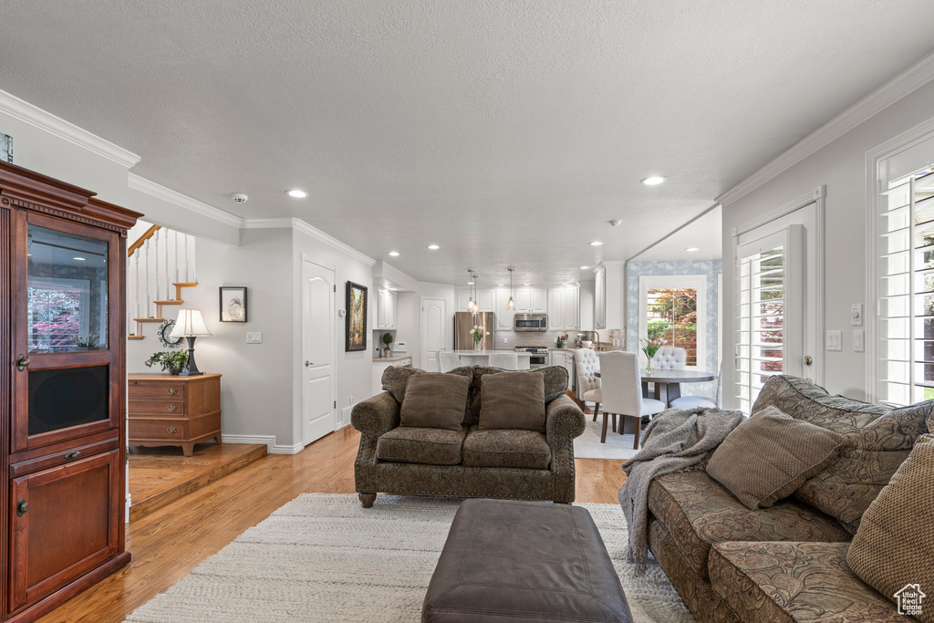 Living area with healthy amount of natural light, light wood-type flooring, crown molding, recessed lighting, and stairway