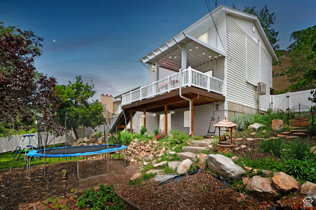 Rear view of property featuring a trampoline, a deck, a fenced backyard, stairs, and a gate