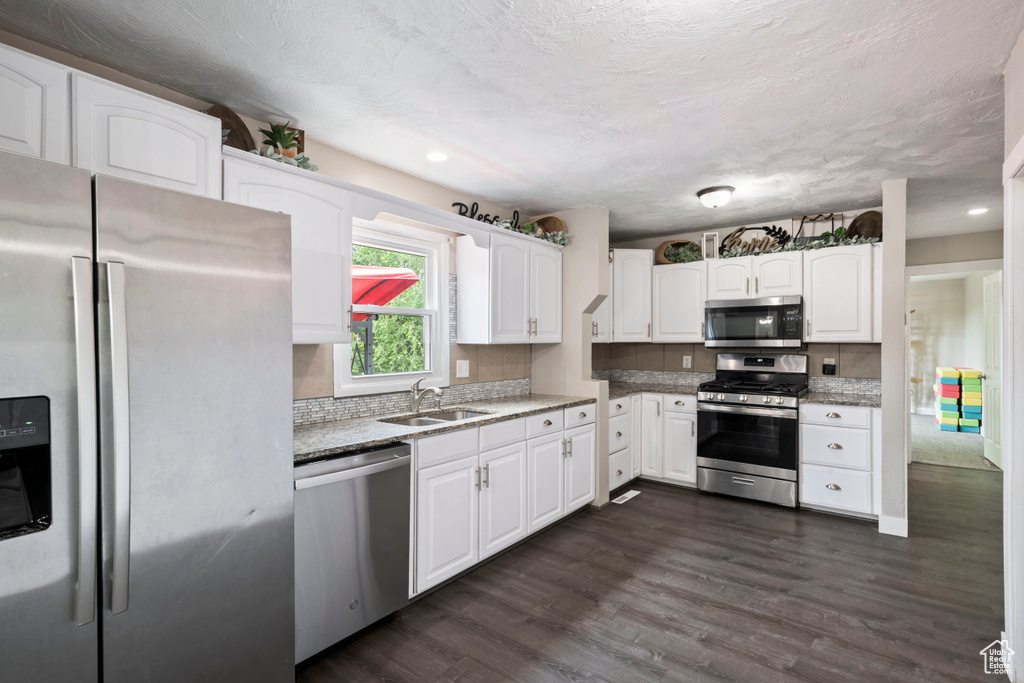 Kitchen with appliances with stainless steel finishes, a sink, white cabinetry, dark wood-type flooring, and tasteful backsplash