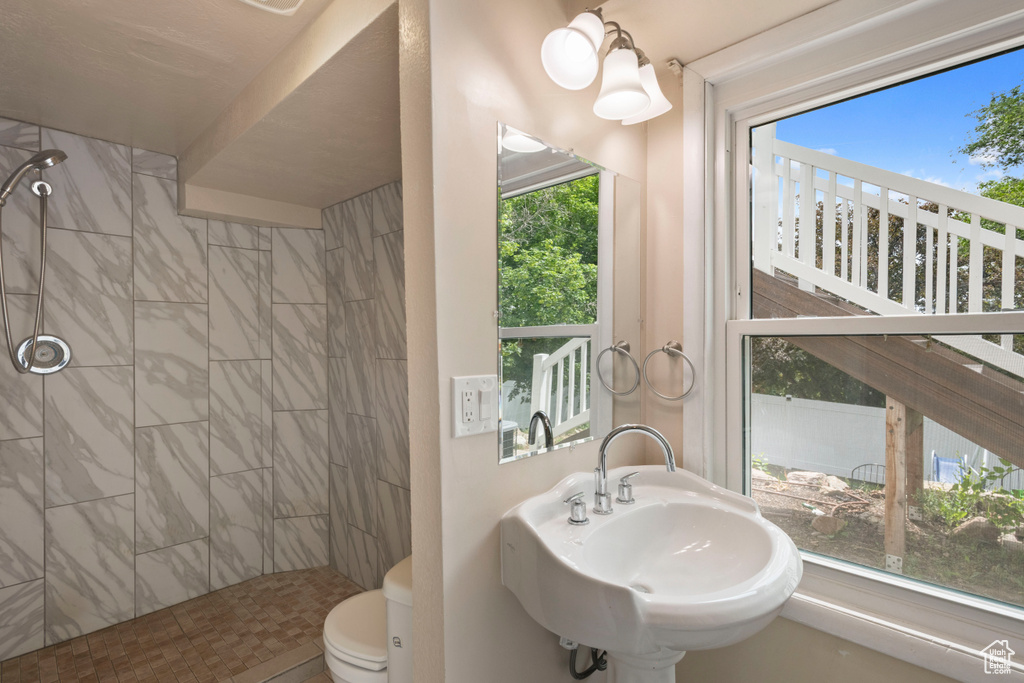 Bathroom with tiled shower, plenty of natural light, toilet, and a sink