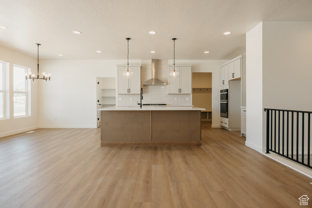 Kitchen with wall chimney range hood, decorative backsplash, stainless steel double oven, light wood finished floors, and recessed lighting