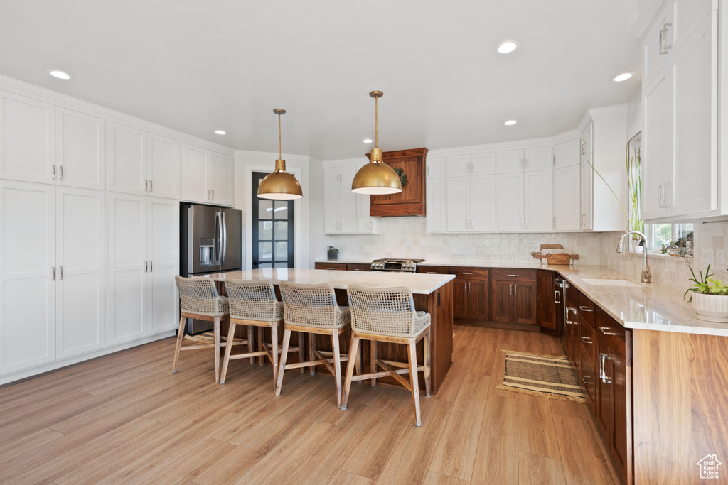 Kitchen featuring a sink, stainless steel refrigerator with ice dispenser, light wood finished floors, white cabinetry, and recessed lighting