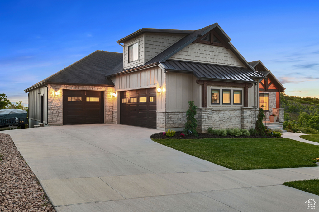 View of front of property with an attached garage, a lawn, board and batten siding, and stone siding