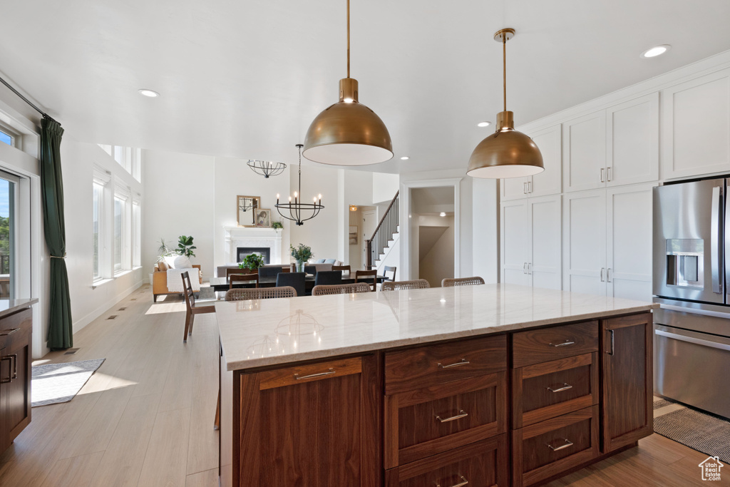 Kitchen featuring stainless steel fridge with ice dispenser, light wood-style floors, light stone countertops, decorative light fixtures, and recessed lighting