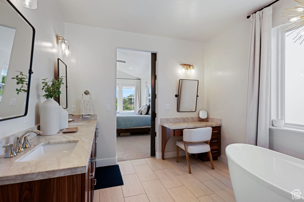 Ensuite bathroom with double vanity, a soaking tub, and baseboards