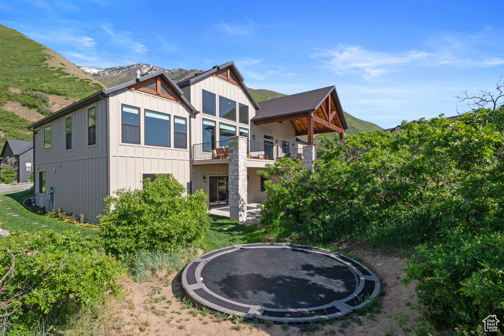 Back of property with a trampoline, a balcony, and a mountain view