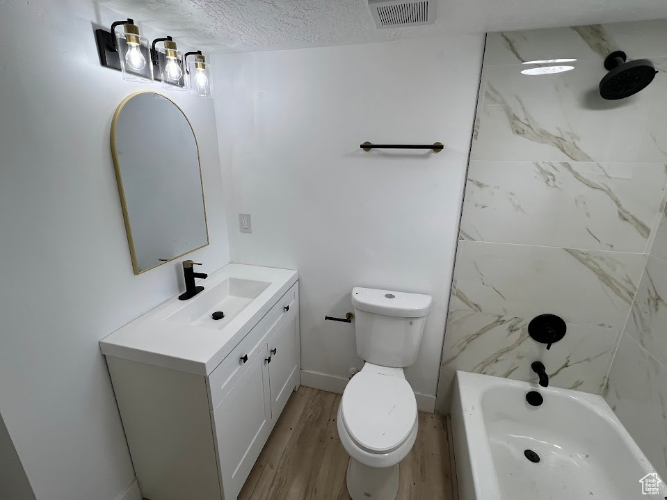 Bathroom featuring toilet, vanity, wood finished floors, a textured ceiling, and tub / shower combination