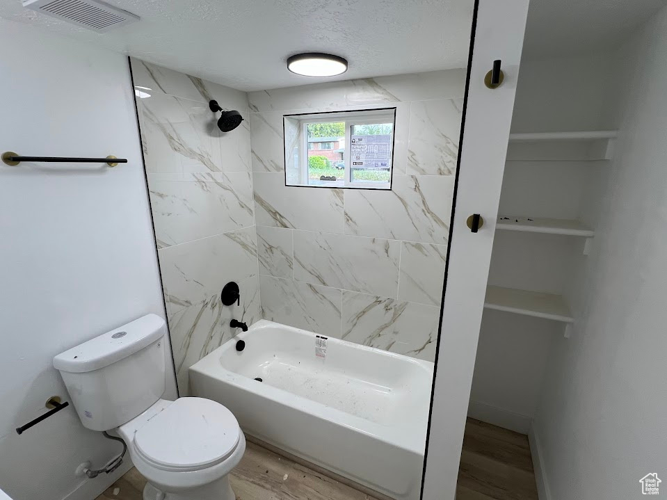 Bathroom with toilet, shower / bath combination, wood finished floors, and a textured ceiling