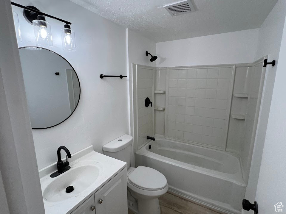 Bathroom featuring toilet, vanity, bathtub / shower combination, wood finished floors, and a textured ceiling