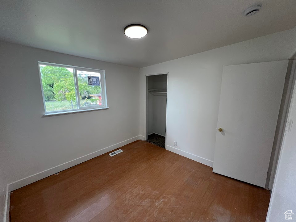 Unfurnished bedroom featuring wood finished floors, baseboards, and a closet