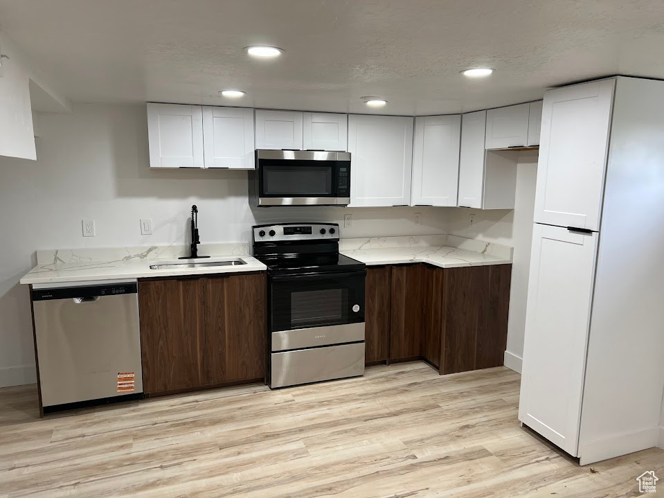 Kitchen featuring appliances with stainless steel finishes, a sink, white cabinets, light stone counters, and recessed lighting