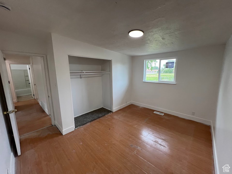 Unfurnished bedroom with wood finished floors, baseboards, and a closet