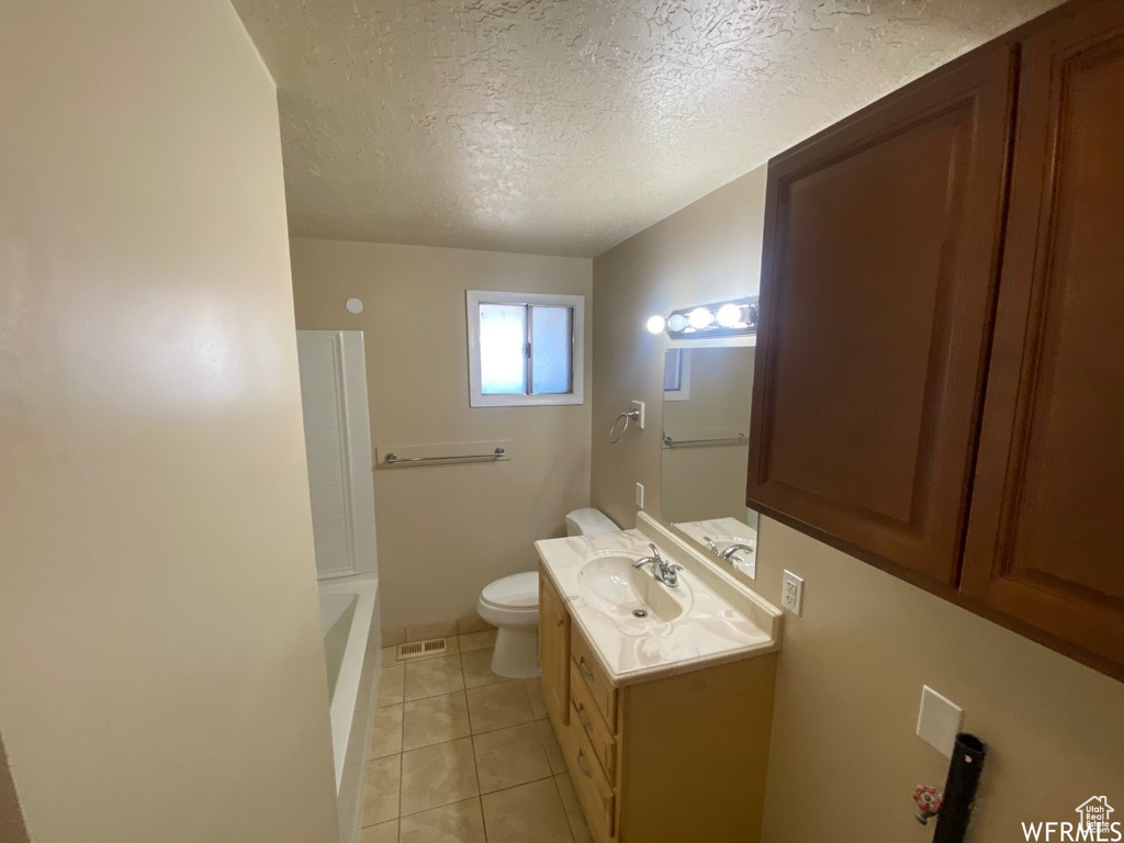 Bathroom featuring a textured ceiling, vanity, toilet, and tile patterned flooring
