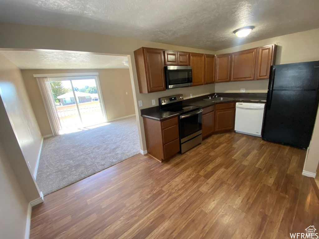 Kitchen with appliances with stainless steel finishes, dark countertops, dark wood finished floors, a textured ceiling, and a sink