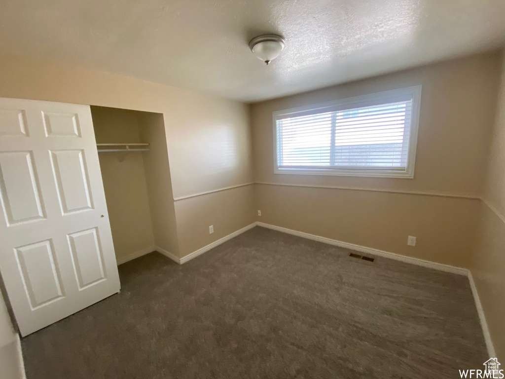 Unfurnished bedroom featuring dark colored carpet, a closet, and baseboards