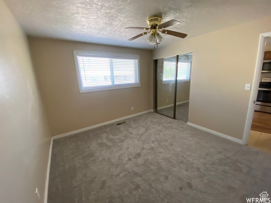 Unfurnished bedroom with carpet floors, a closet, baseboards, a textured ceiling, and a ceiling fan