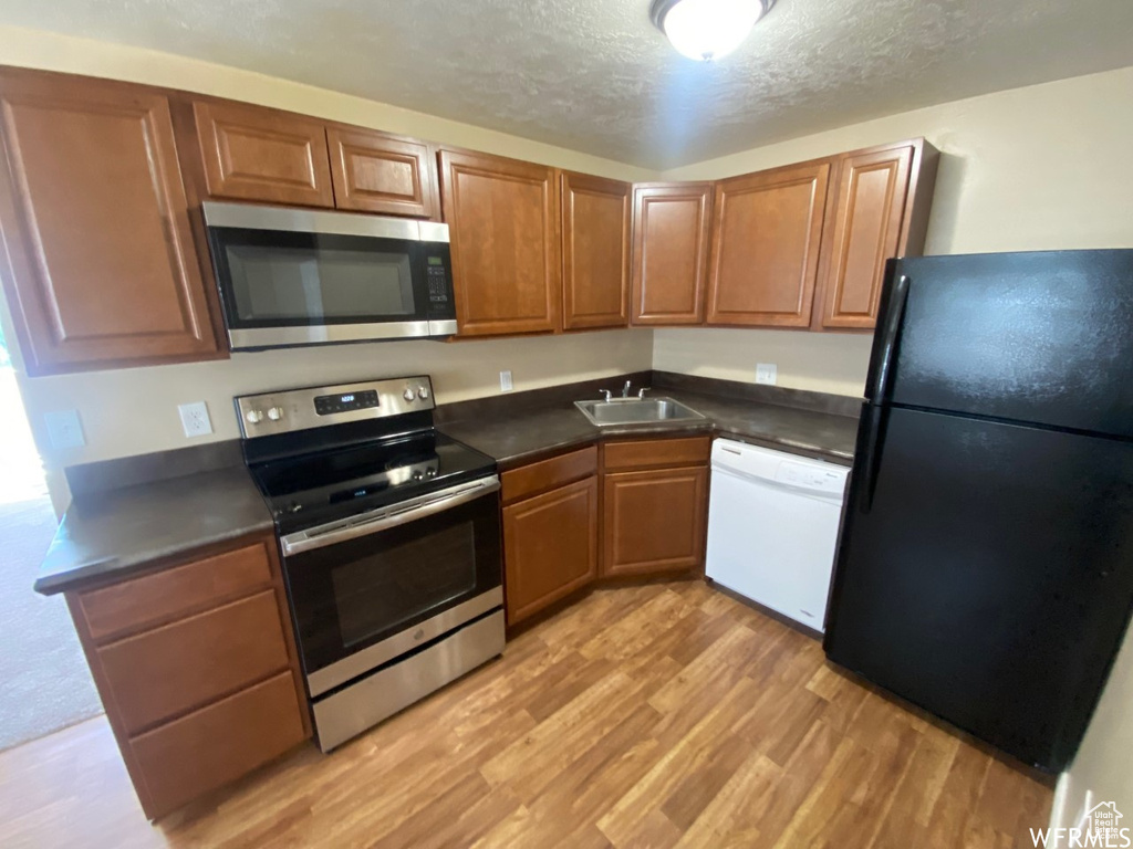 Kitchen featuring stainless steel appliances, light wood-type flooring, a sink, dark countertops, and brown cabinets