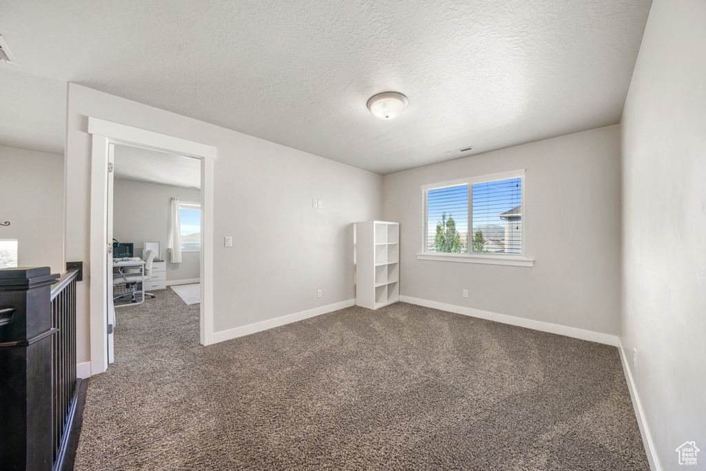 Unfurnished bedroom with dark carpet, baseboards, and a textured ceiling