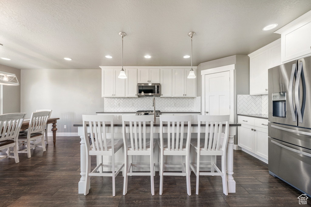Kitchen with appliances with stainless steel finishes, tasteful backsplash, an island with sink, a breakfast bar area, and recessed lighting