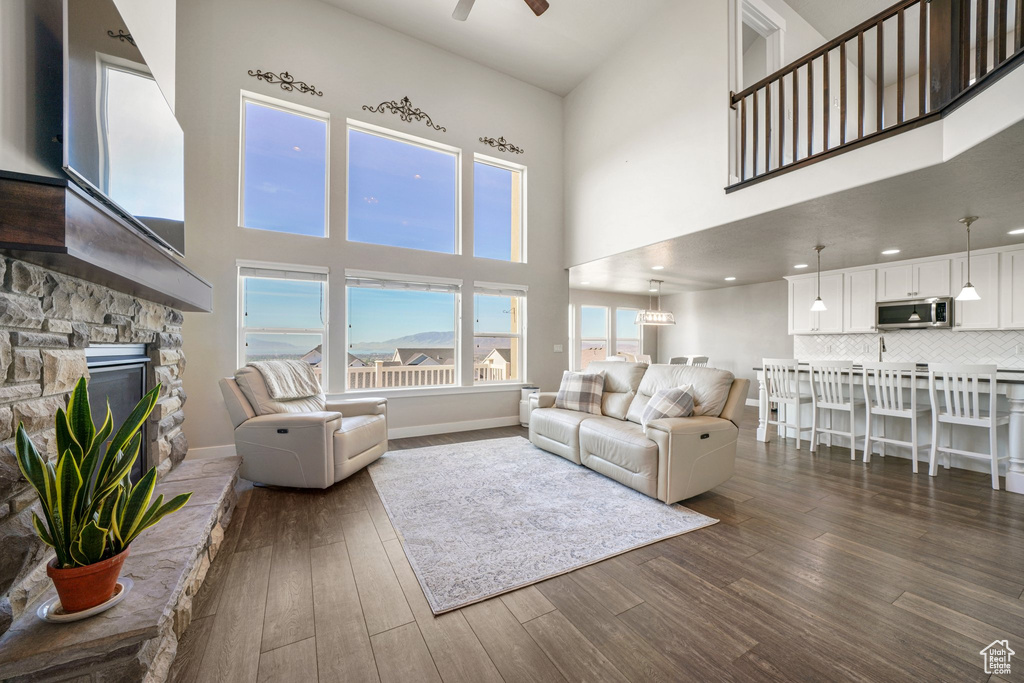 Living room with a high ceiling, a fireplace, a ceiling fan, dark wood finished floors, and baseboards