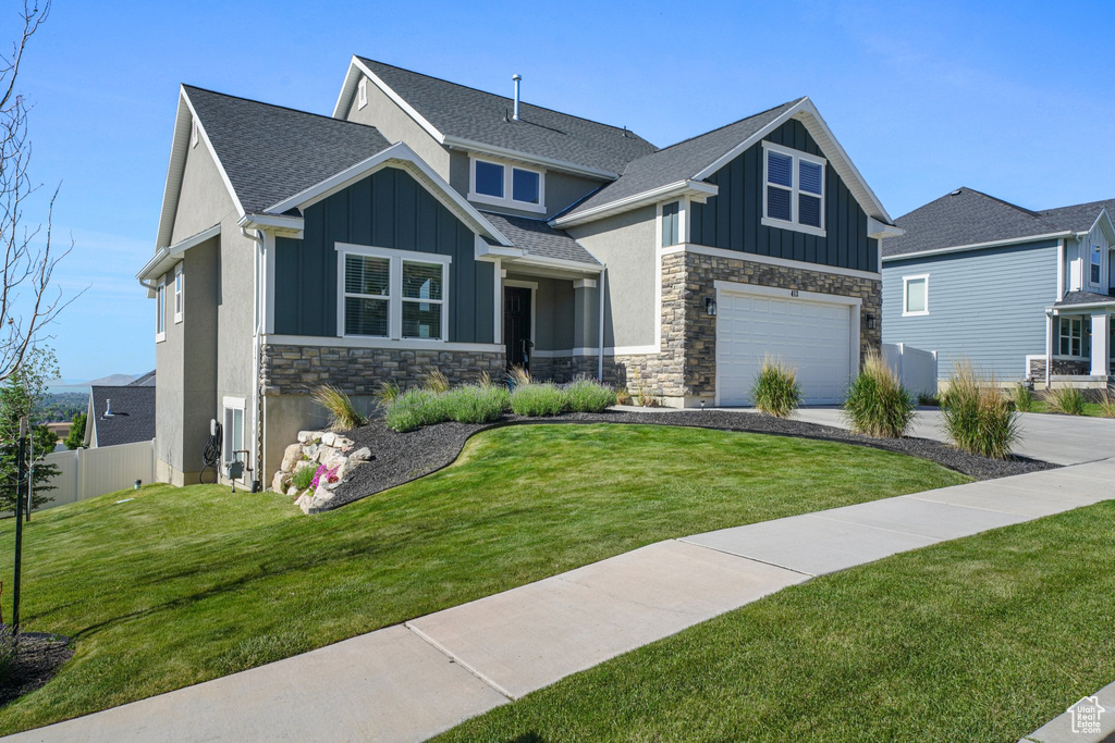 Craftsman-style home featuring stone siding, board and batten siding, an attached garage, driveway, and a shingled roof