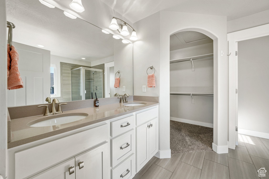 Full bathroom with a shower stall, double vanity, a walk in closet, and baseboards