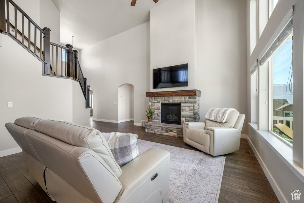 Living area with a towering ceiling, dark wood-style floors, a stone fireplace, arched walkways, and a ceiling fan