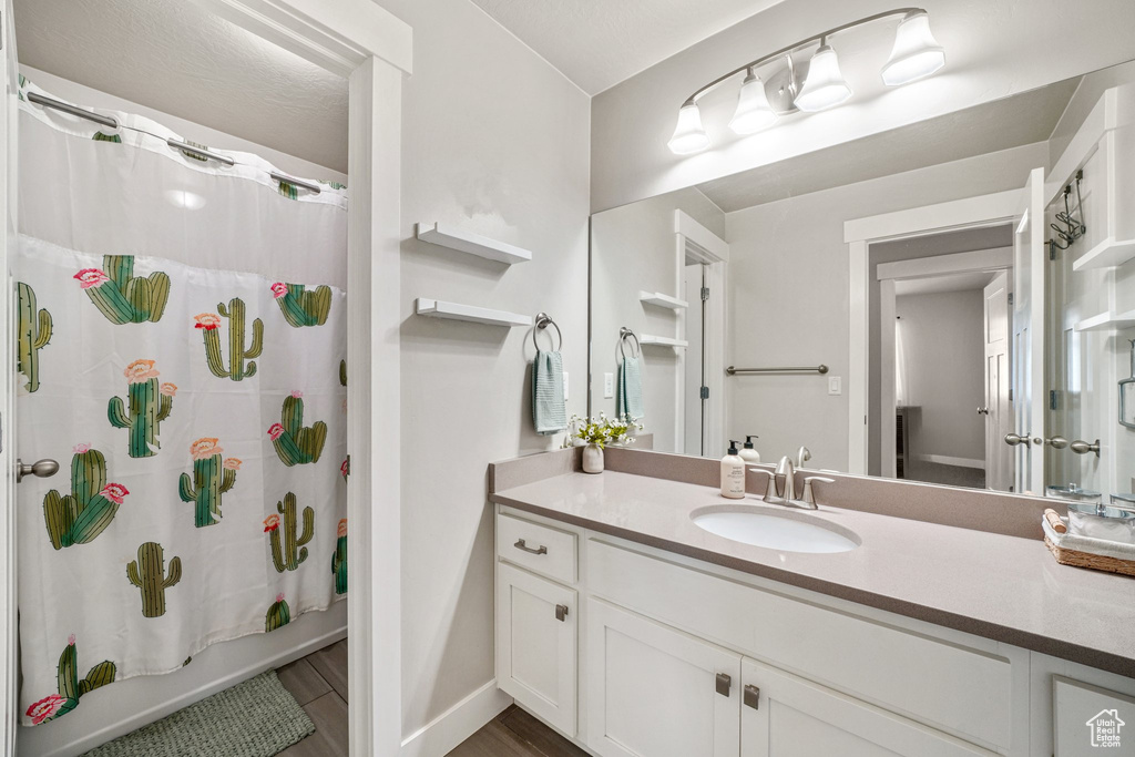 Bathroom featuring vanity, shower / bathtub combination with curtain, wood finished floors, and baseboards
