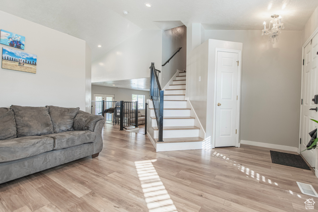 Living area with baseboards, stairs, light wood-style flooring, a chandelier, and high vaulted ceiling