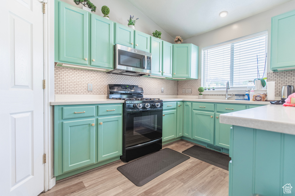 Kitchen with stainless steel microwave, black gas range oven, a sink, decorative backsplash, and light countertops