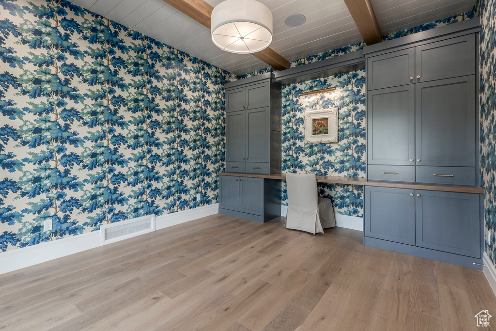 Unfurnished office featuring wallpapered walls, light wood-type flooring, wooden ceiling with exposed beams, and baseboards