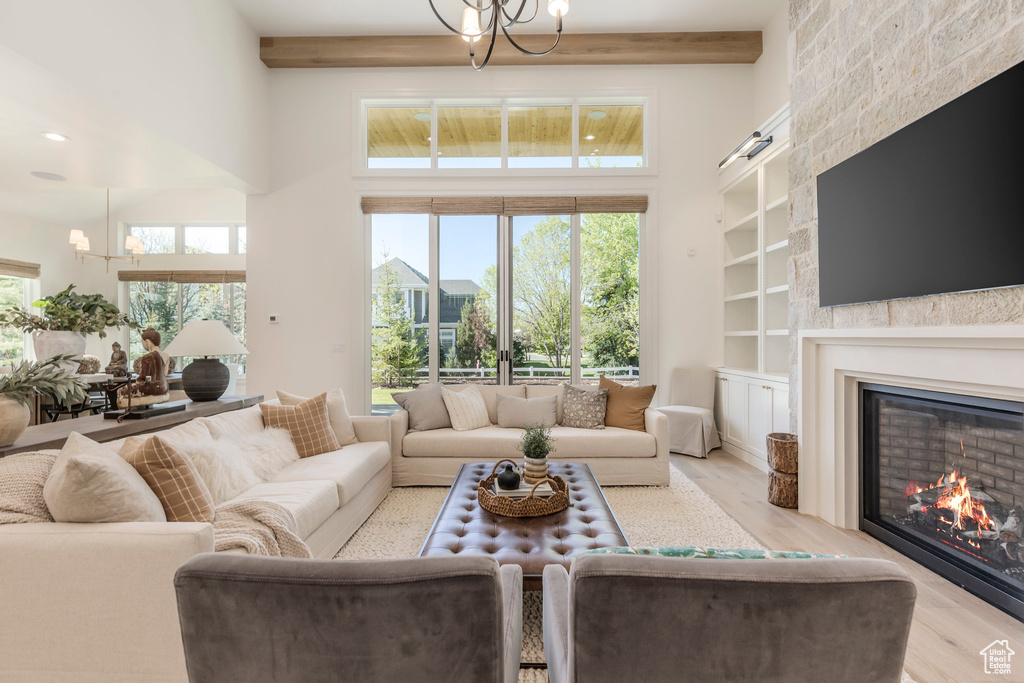 Living room featuring a high ceiling, a fireplace, light wood-style flooring, built in shelves, and beam ceiling