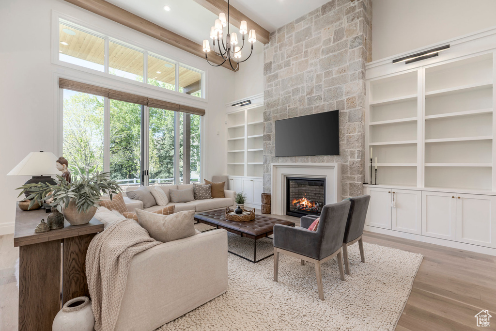Living room with a high ceiling, a stone fireplace, built in features, light wood-style floors, and beam ceiling
