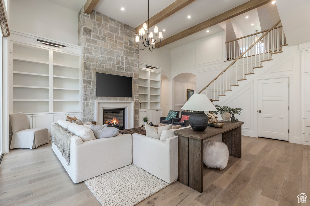 Living room featuring arched walkways, beam ceiling, light wood-type flooring, stairway, and a stone fireplace