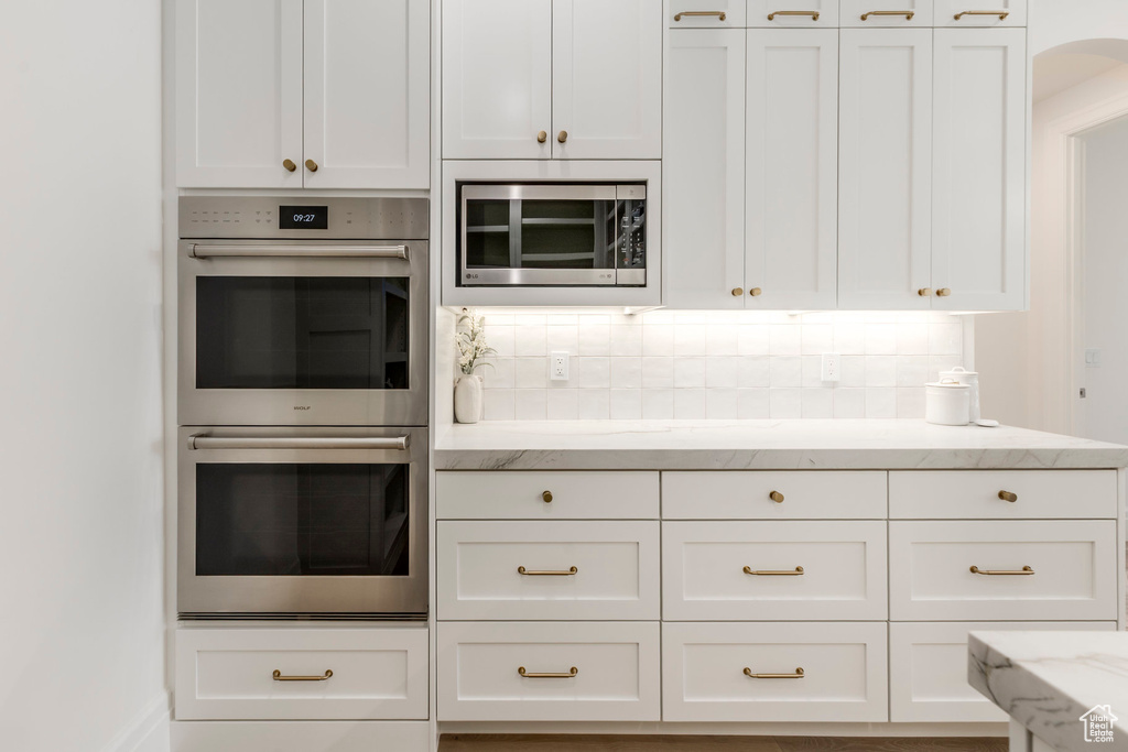 Kitchen featuring stainless steel appliances, white cabinets, light stone counters, and backsplash