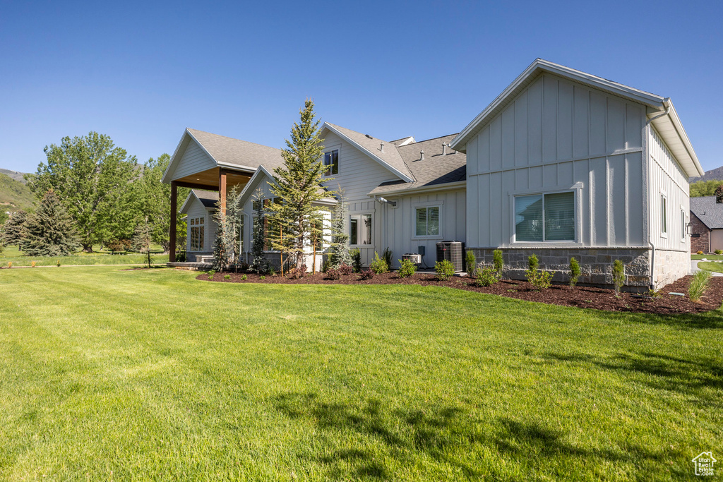 View of front of house featuring board and batten siding, a front yard, a shingled roof, and central air condition unit
