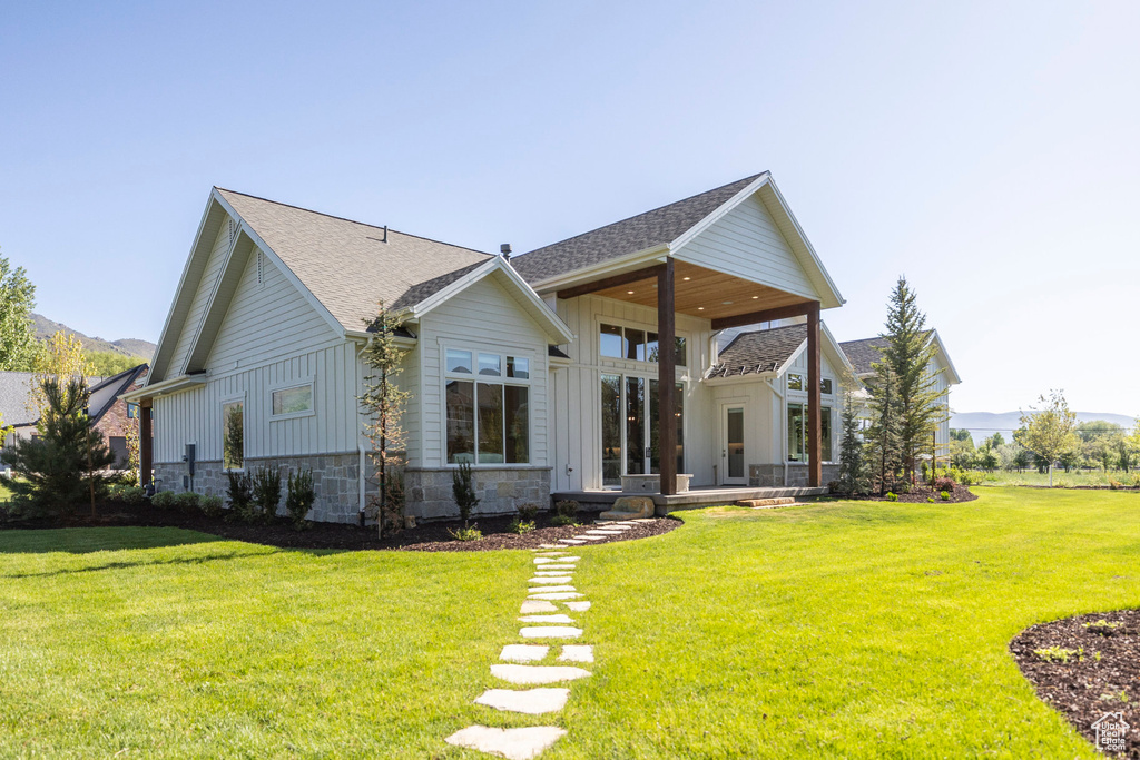 Rear view of property featuring board and batten siding, a yard, stone siding, and roof with shingles